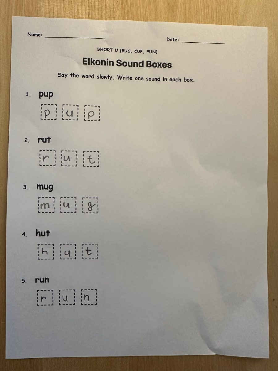A printed Short U Elkonin sound box worksheet with the words pup, rut, mug, hut, and run, each sound written in its own box in a child's handwriting